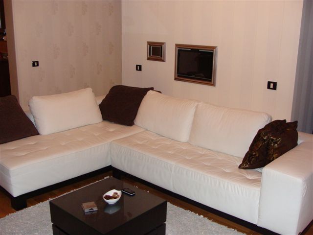 White corner sofa in a modern apartment living room in Budva, Montenegro: stylish interior with a dark coffee table.