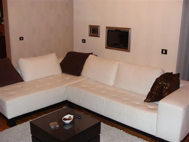 White L-shaped sofa with brown cushions, black coffee table on a light rug against plain walls.
