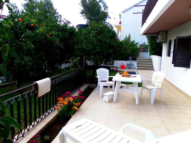 House terrace in Herceg Novi, Montenegro: plastic furniture, view of the garden with citrus trees, and tiled floor.