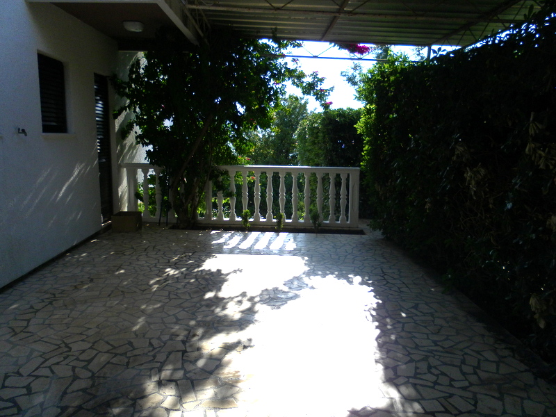 Cozy covered terrace with stone floor and balustrade in a house in Herceg Novi, Montenegro, surrounded by greenery.