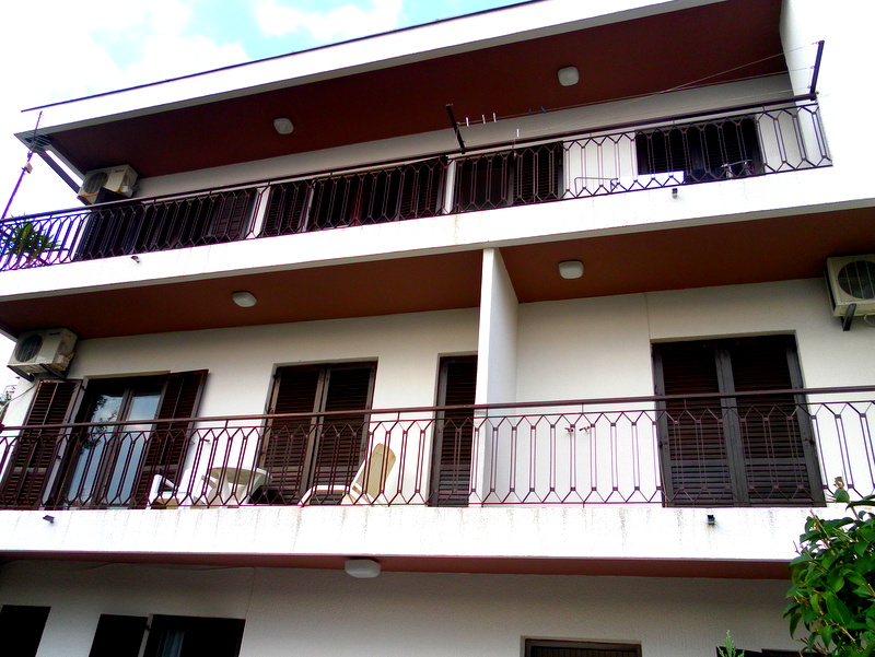 House facade in Herceg Novi, Montenegro: white walls, open balconies with wrought-iron railings and brown shutters.