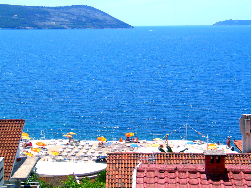 Panoramic view of the sea and beach from the house terrace in Herceg Novi, Montenegro, with tiled roofs in the foreground.