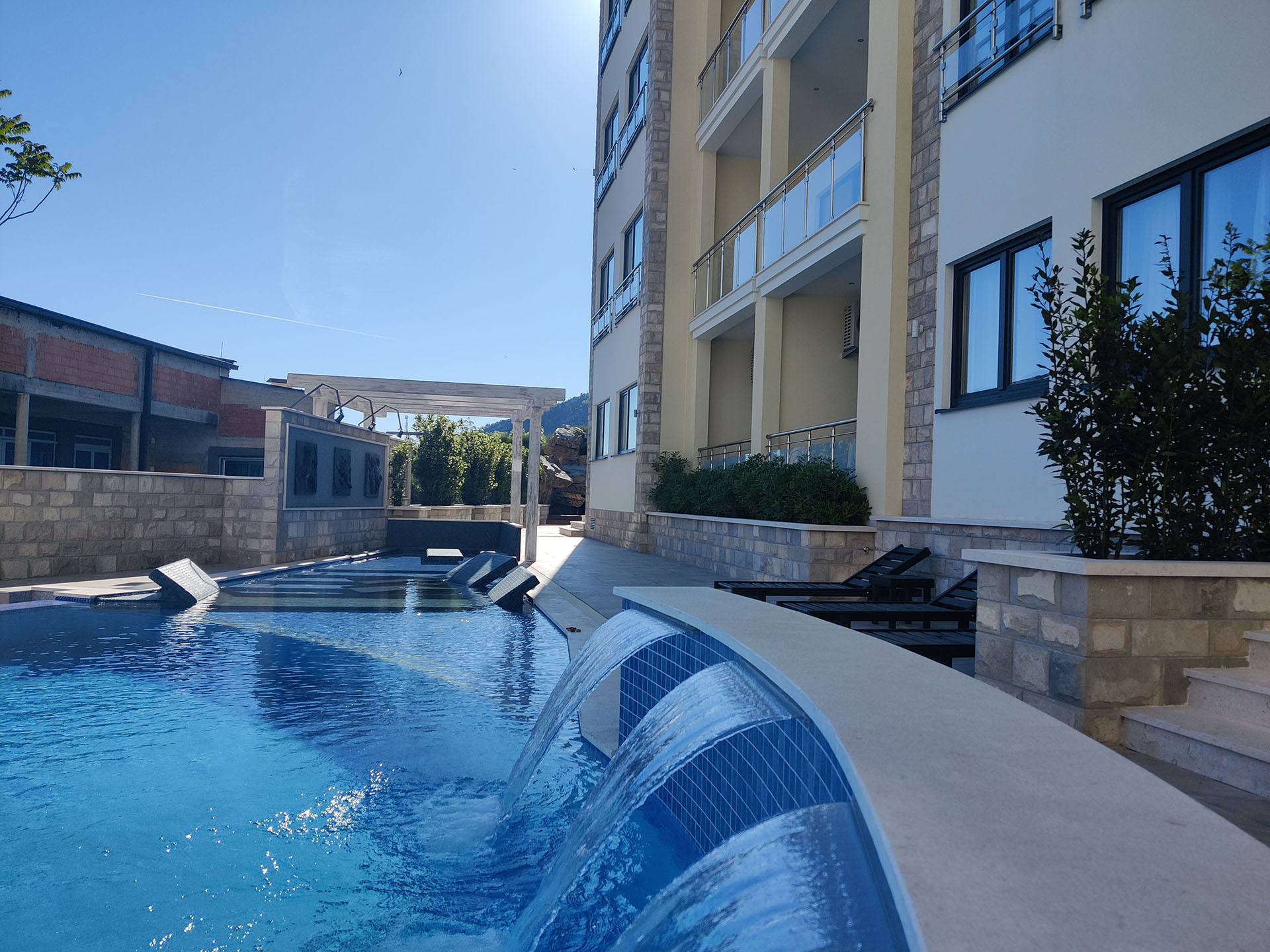 Swimming pool with a waterfall and sun loungers at the MonteDreams residential complex in Bečići, Budva Riviera, Montenegro.