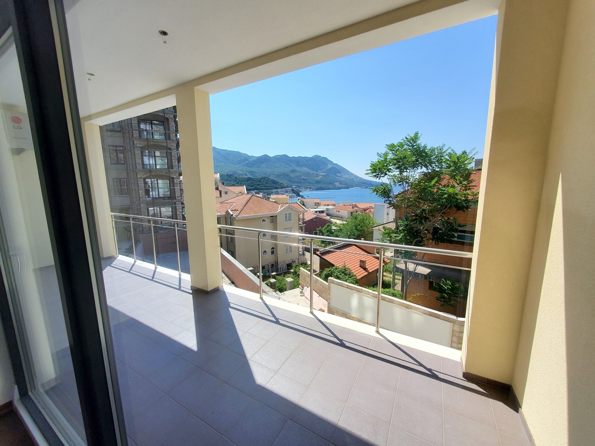 Spacious balcony with sea and mountain views in MonteDreams residential complex, Becici, Montenegro: tiled floor and glass railings.