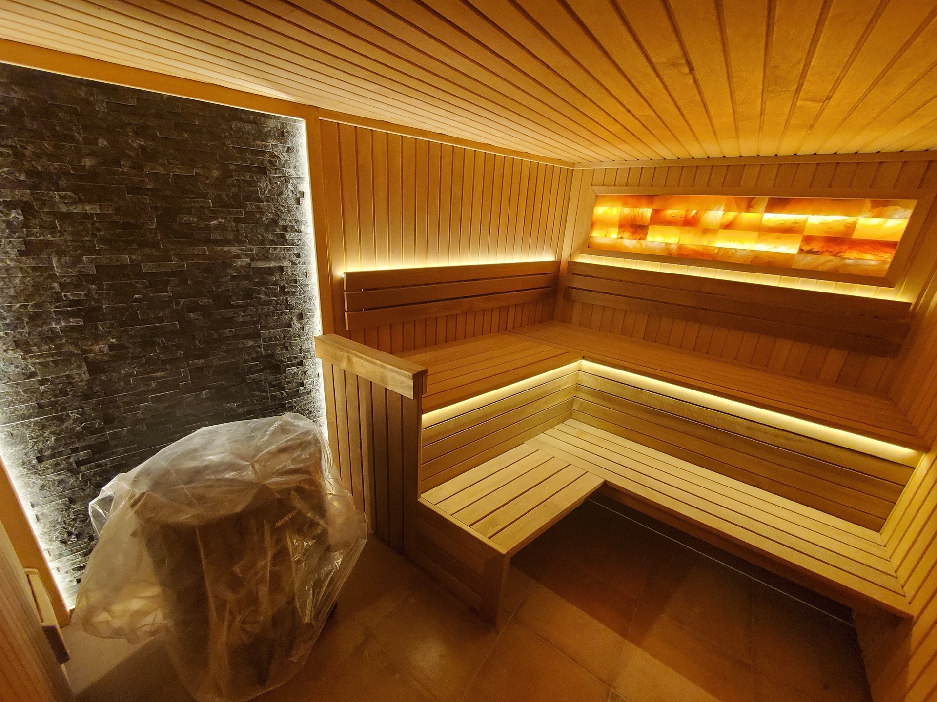 Modern sauna with wood finish, Himalayan salt lighting, and a stone wall in MonteDreams residential complex, Becici, Montenegro
