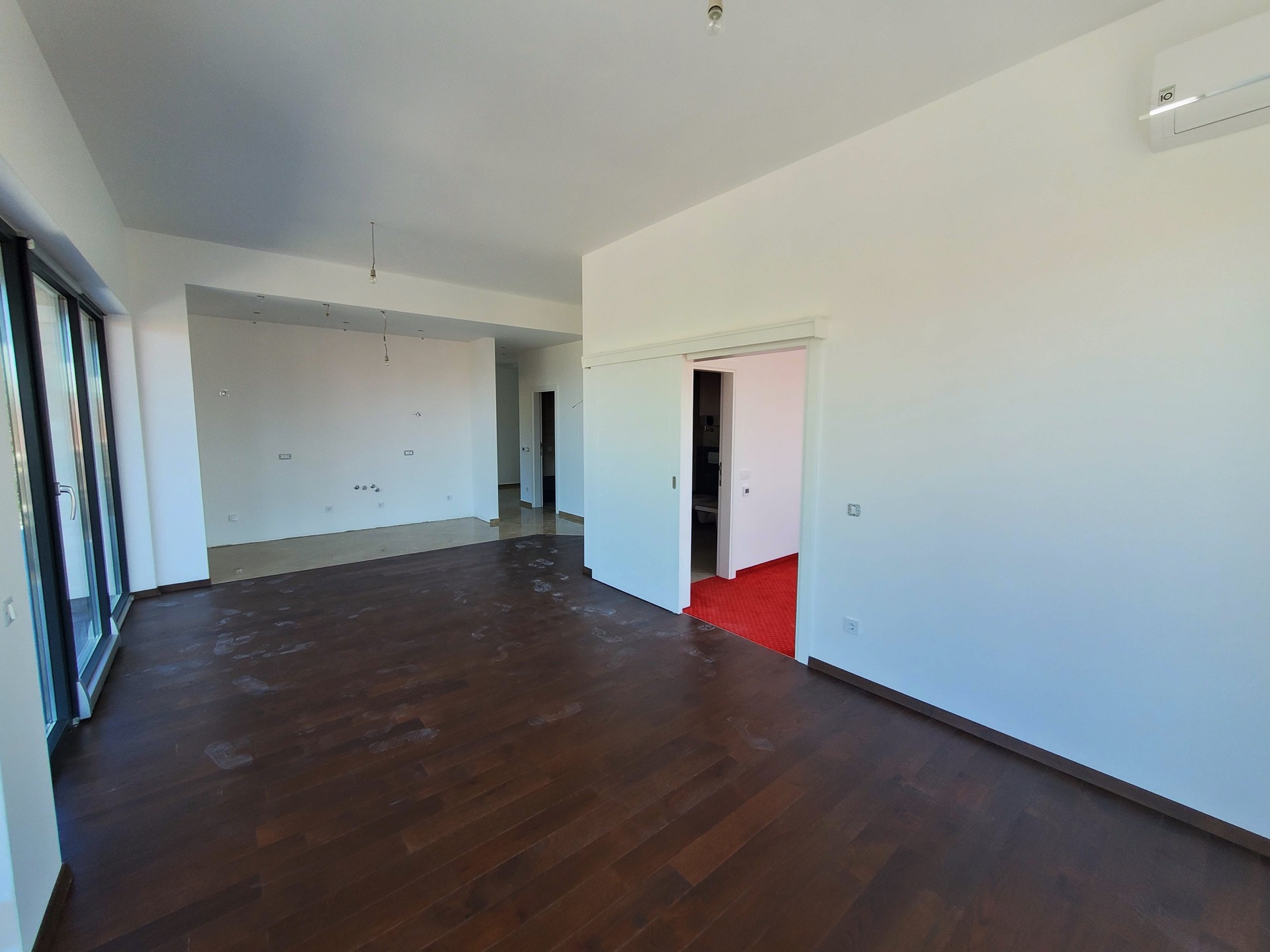 Bright living room in MonteDreams, Becici, Montenegro: dark parquet flooring, panoramic windows, and sliding doors.