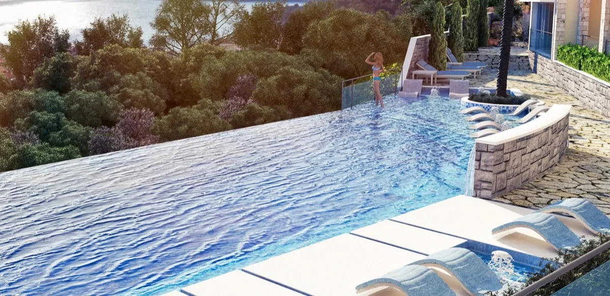 Infinity pool with waterfalls and loungers overlooking a forest and sea.