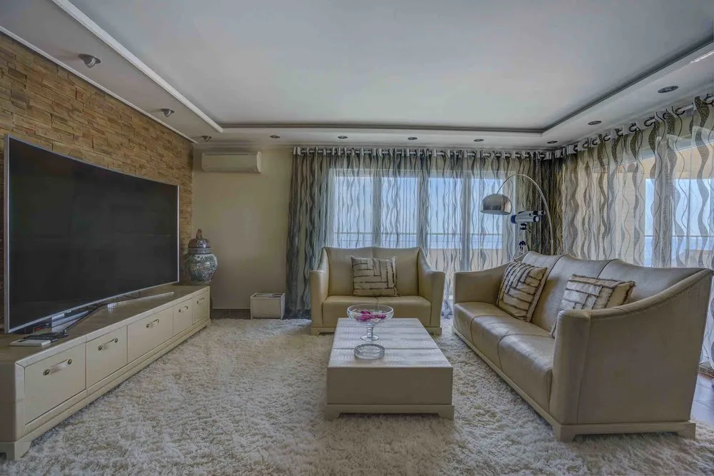 Living room with beige sofa, large TV on stone wall, and white shag rug.