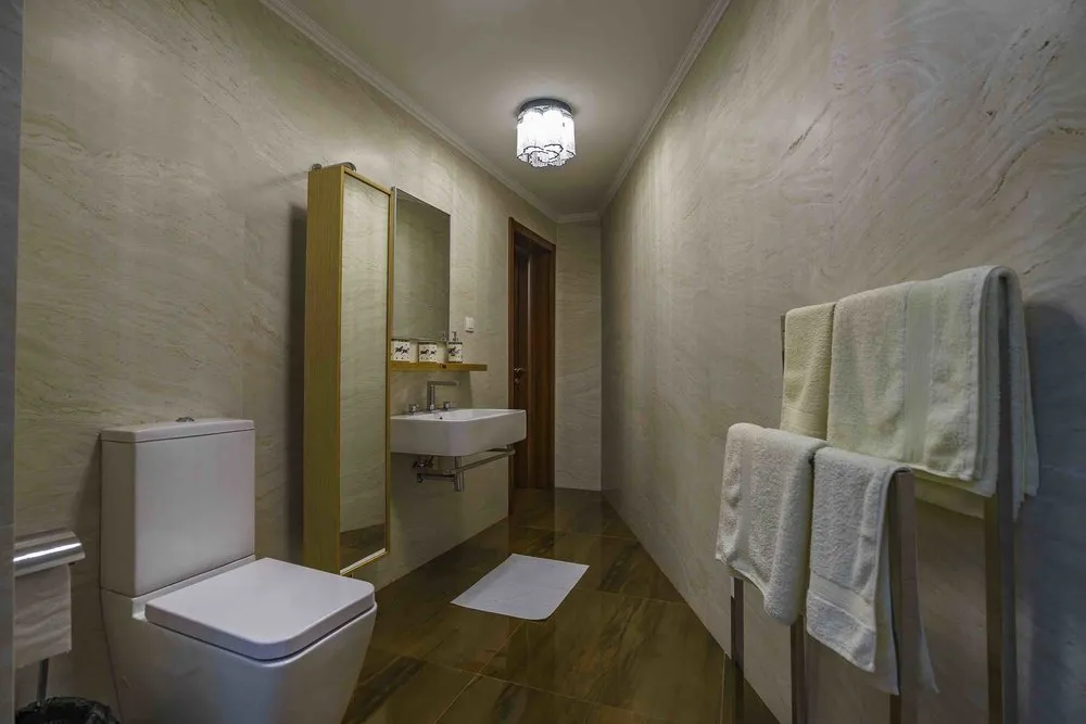 Bathroom featuring a white toilet, wall-mounted sink, wooden-framed mirror, and a towel rack with towels.