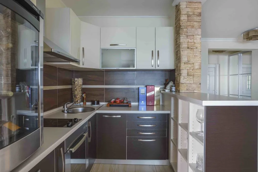 Modern kitchen with white and dark cabinets, built-in appliances, sink, and a stone-clad pillar.