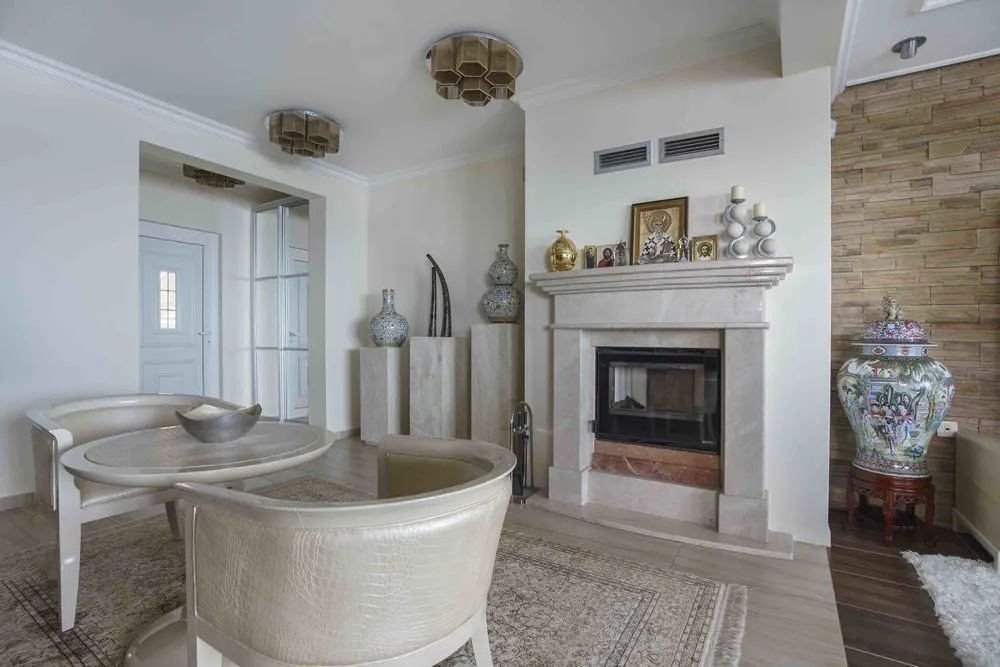 Living room featuring a marble fireplace, round table with curved chairs, and decorative vase against a stone wall.