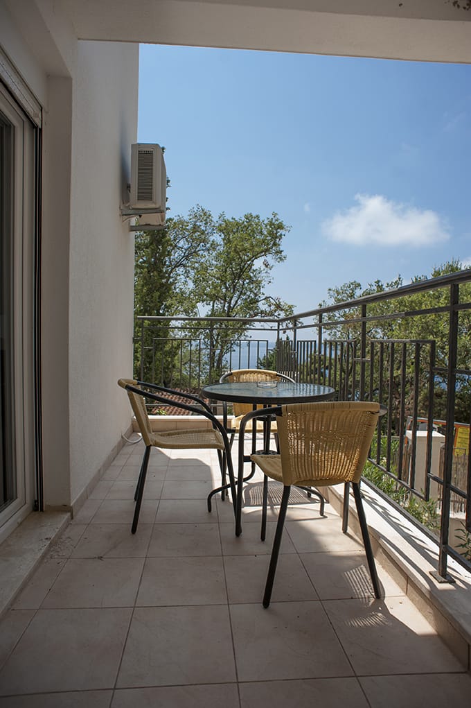 Balcony with wicker furniture and sea view at a villa in Perazica Do, Montenegro. Cozy terrace with dining area.