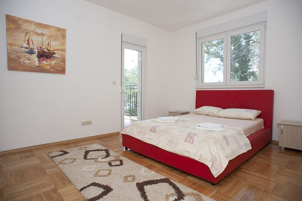 Bright bedroom with a red double bed and access to the balcony in a villa in Perazica Do, Montenegro.