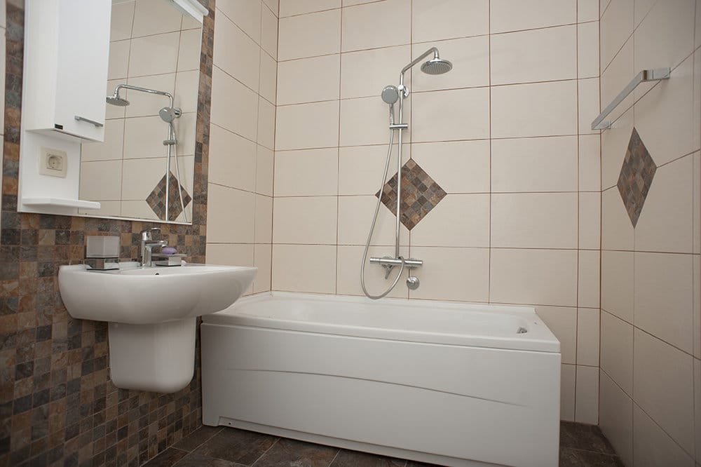 Bathroom featuring a white bathtub, shower system, wall-mounted sink, and mirror on tiled walls.