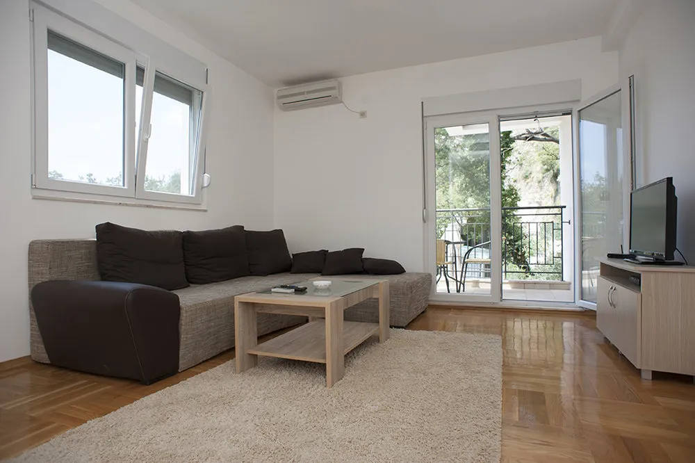 Living room with grey sofa, wooden table, rug, and glass door leading to a balcony.