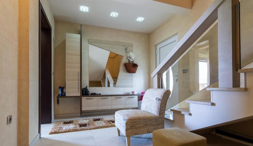 Modern hallway in a villa in Tivat, Montenegro: light-colored furniture, mirror, staircase with glass railing.