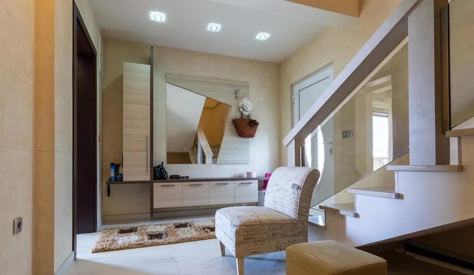 Entryway with staircase, large mirror, storage unit, and patterned armchair.
