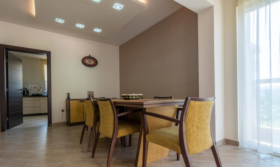 Modern living room with dining area in a villa in Tivat, Montenegro: wooden table, yellow chairs, and recessed lighting.