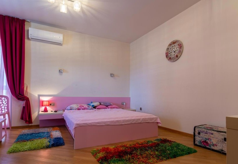Bedroom with a pink bed and bright rugs in a villa in Tivat, Montenegro. Light finishes, air conditioning, and decor.