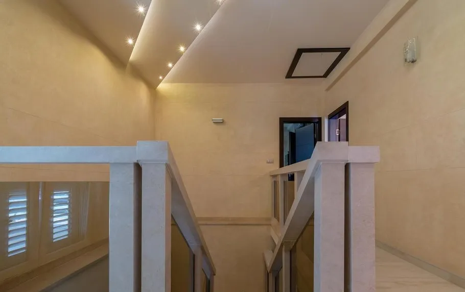 Interior staircase with stone railings, glass panels, and recessed spotlights in a dropped ceiling niche.