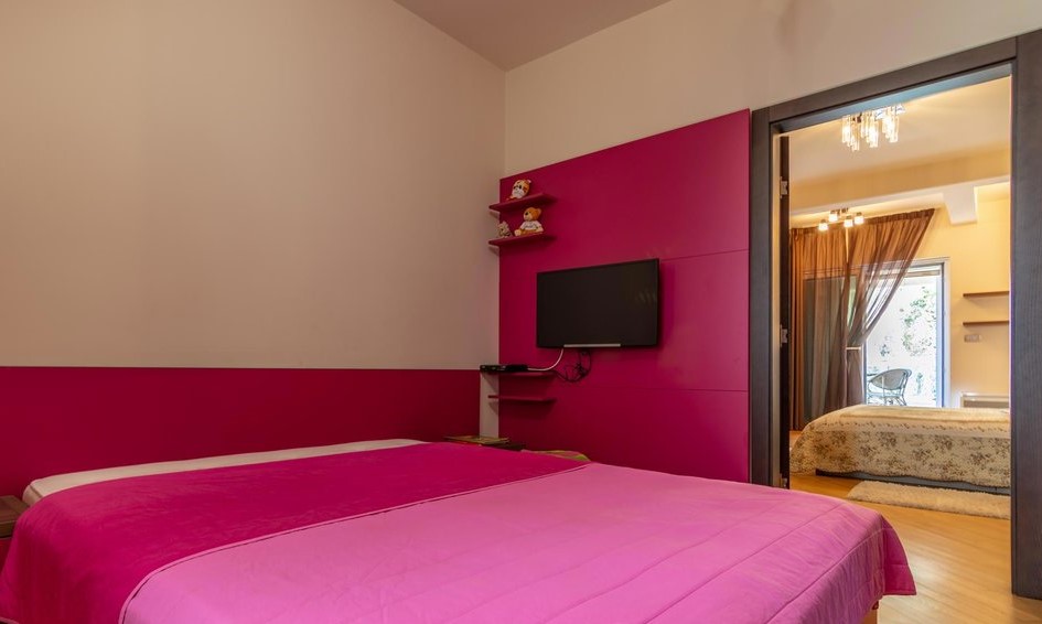 Bedroom with bright pink decor and a double bed in a villa in Tivat, Montenegro, view into the adjoining room.