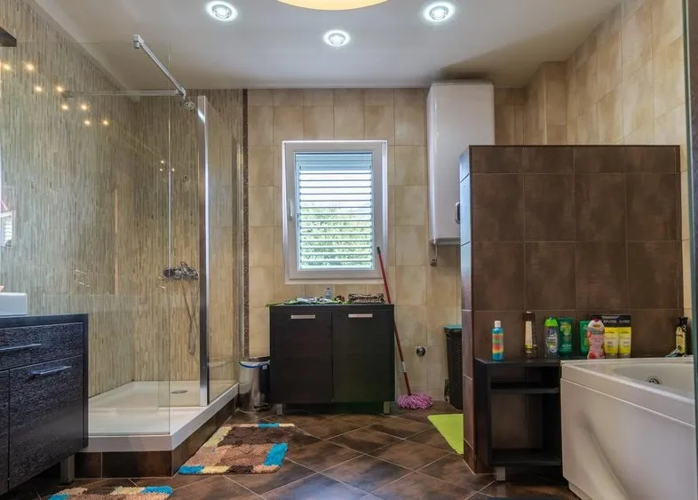 Bathroom with glass shower, bathtub, dark cabinet, and tiled walls.