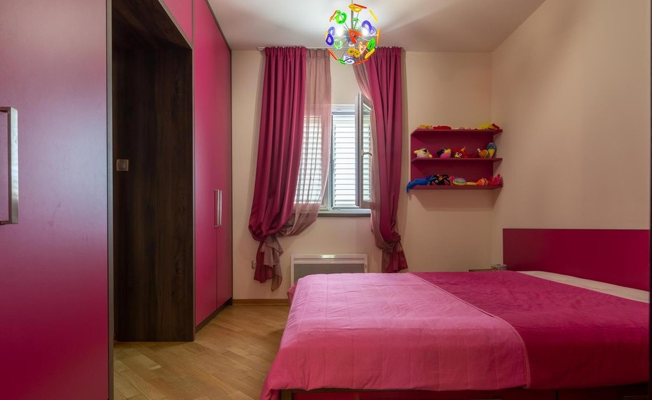 Bright children's bedroom with pink furniture and a bed in a villa in Tivat, Montenegro. Parquet floor, window with curtains.