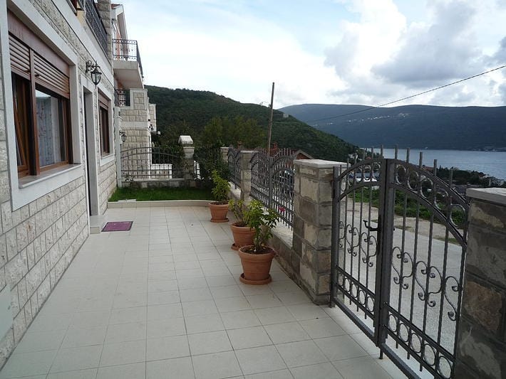 Terrace of a house in Zelenika, Montenegro: stone finish, wrought-iron gates, potted plants, and a view of the Bay of Kotor.
