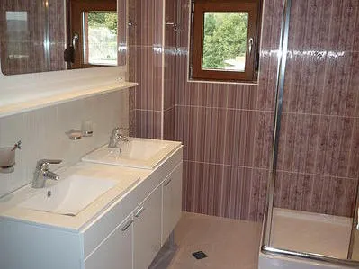 Bathroom featuring a double sink vanity, white cabinet, large mirror, and glass shower enclosure against pink tiles.