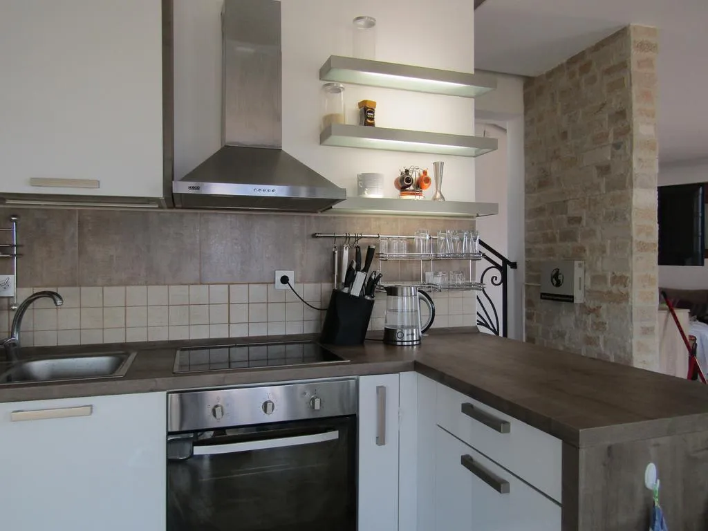 Modern kitchen featuring white cabinets, stainless steel hood, cooktop, sink, and grey countertops with open shelving.