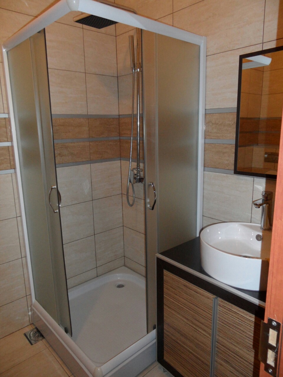 Modern bathroom in an apartment in Budva, Montenegro: shower cabin, vanity with countertop sink, and mirror.
