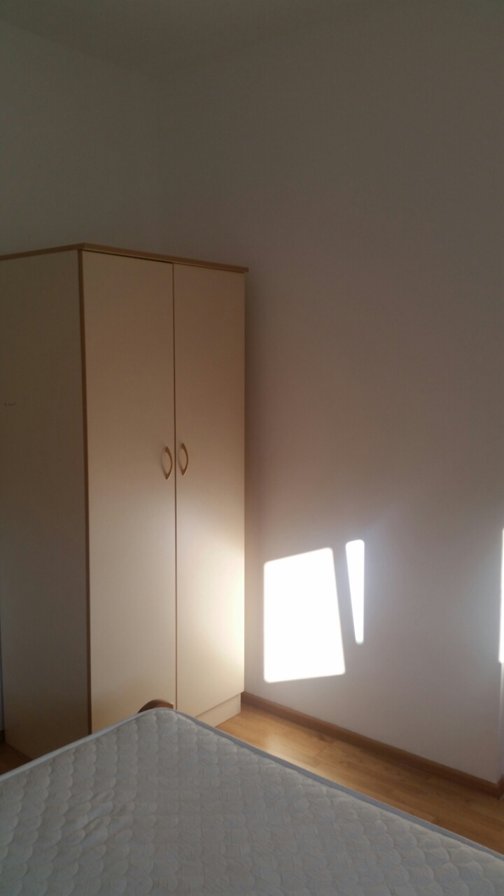 Bright bedroom in an apartment in Budva, Montenegro: a two-door wardrobe, a bed with a mattress, and laminate flooring.