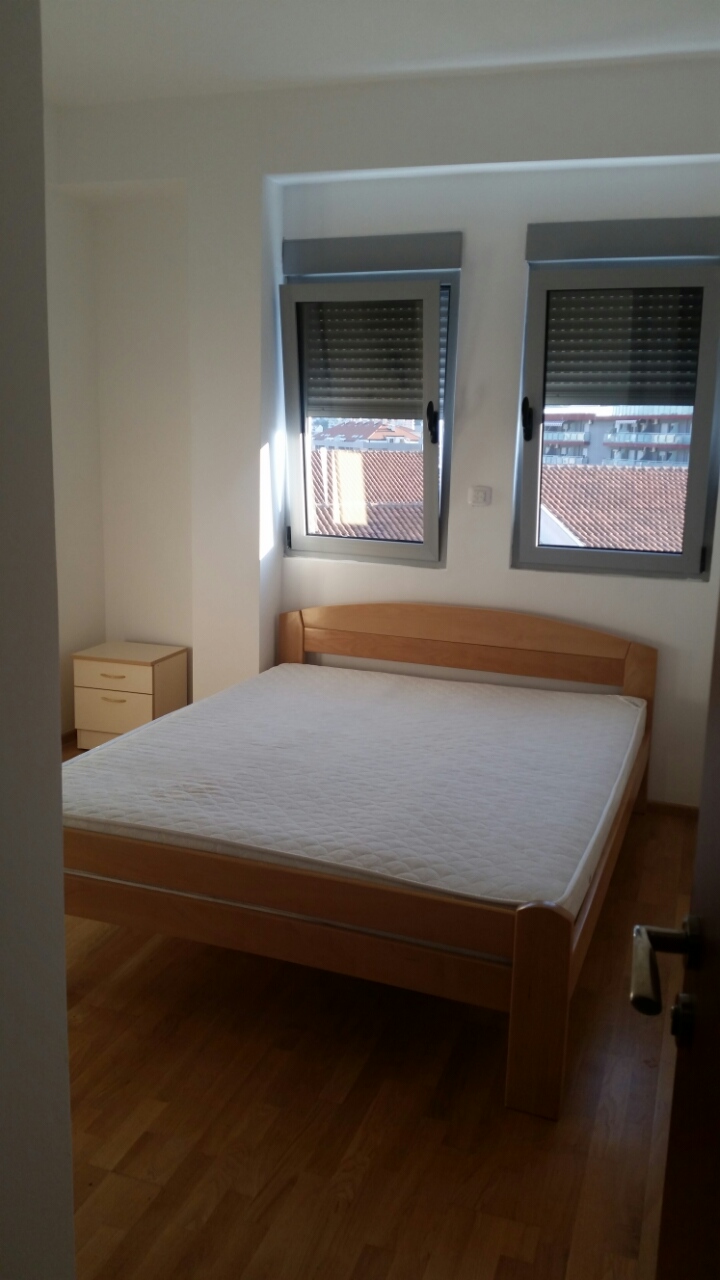 Bright bedroom with a double bed and parquet flooring in an apartment in Budva, Montenegro, with a view of the tiled roofs from the window.
