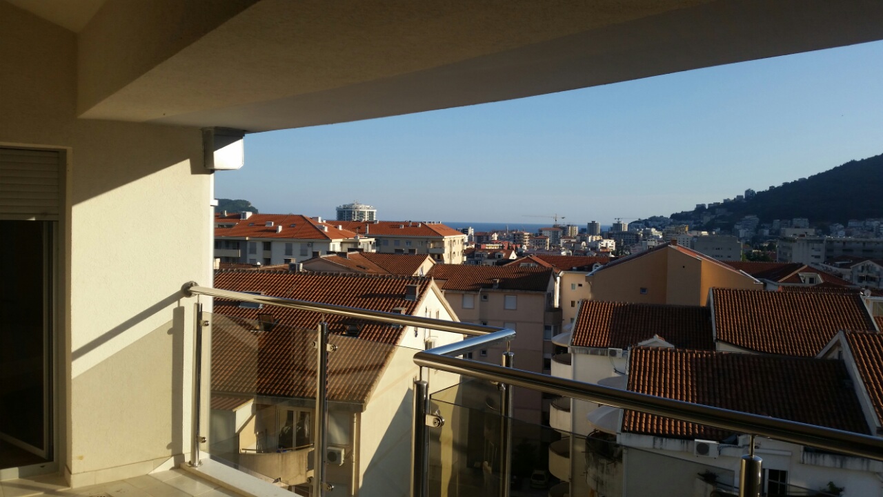 View from the apartment balcony in Budva, Montenegro: a panorama of the city with tiled roofs and the sea horizon.