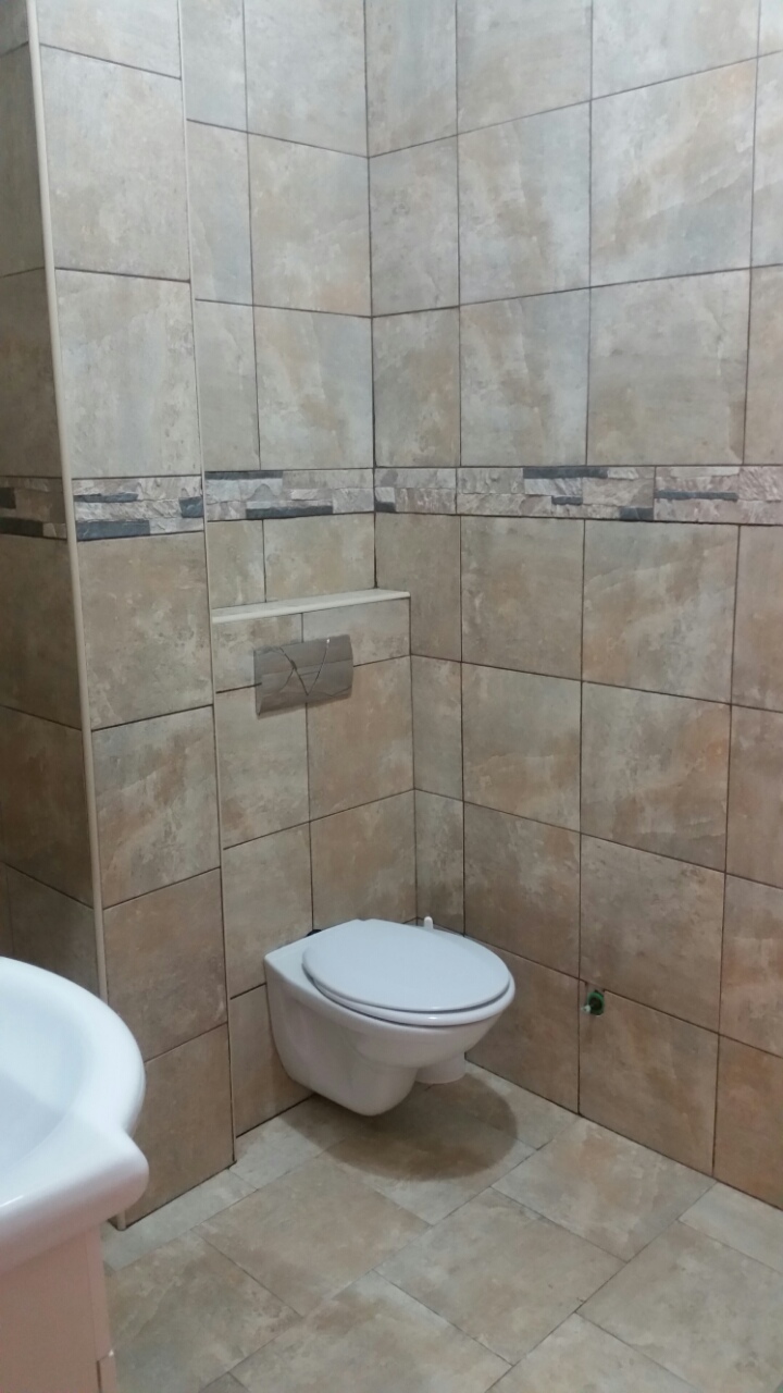 Modern bathroom in an apartment in Budva, Montenegro: wall-mounted toilet and beige stone-look tile finish.