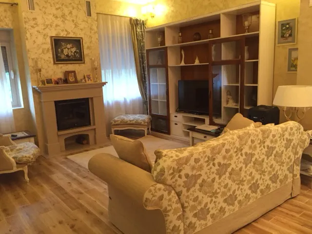 Living room featuring a floral sofa, fireplace, and large display cabinet with TV on wood flooring.