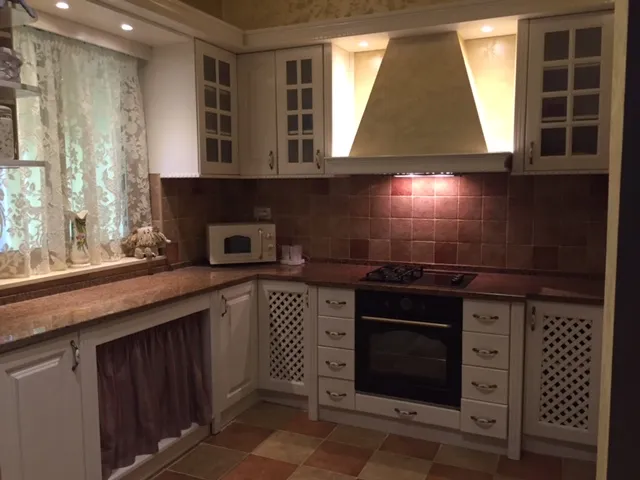Kitchen with white cabinets, black oven, microwave, and brown tiled backsplash under warm lighting.