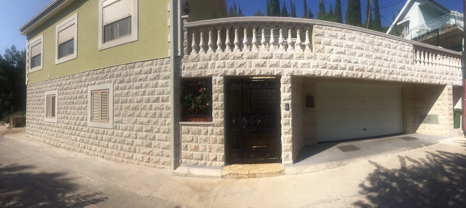 House exterior featuring stone facade, ornate metal entrance door, and white garage door under daylight.