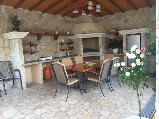 Summer kitchen with barbecue and dining area in the house, Zelenika, Montenegro: stone finish, wooden ceiling and furniture.