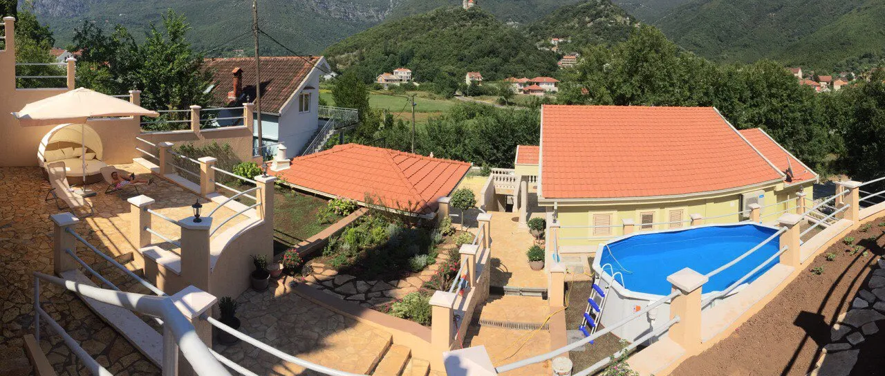 View of a terrace with a pool, garden, and house roofs against mountains.