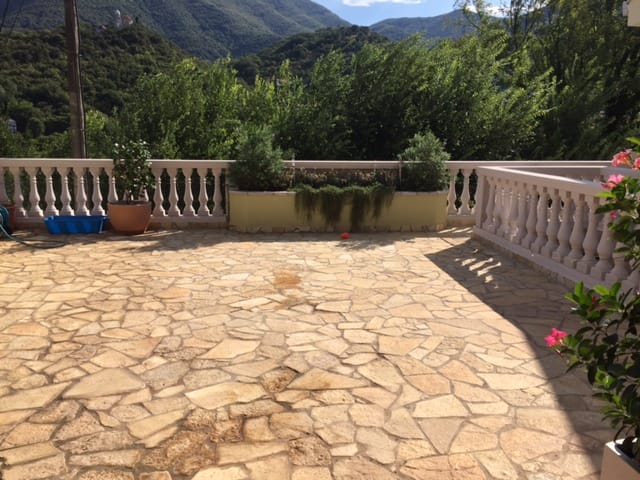 Spacious terrace with stone flooring and balustrade in a house in Zelenika, Montenegro, overlooking green mountains.