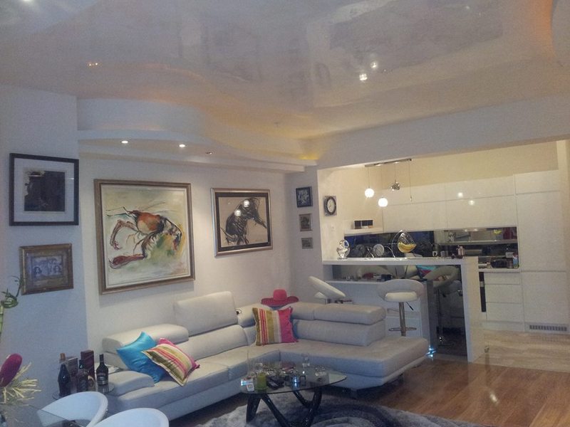 Modern living room with a white corner sofa and kitchen in an apartment in Budva, Montenegro: stylish interior and decor.