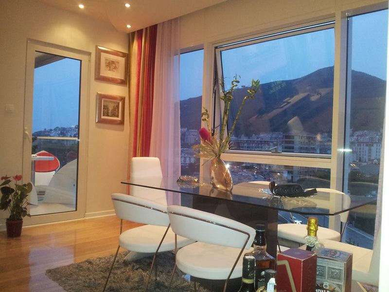 Living room with panoramic windows and mountain views in an apartment, Budva, Montenegro: glass table and white chairs.