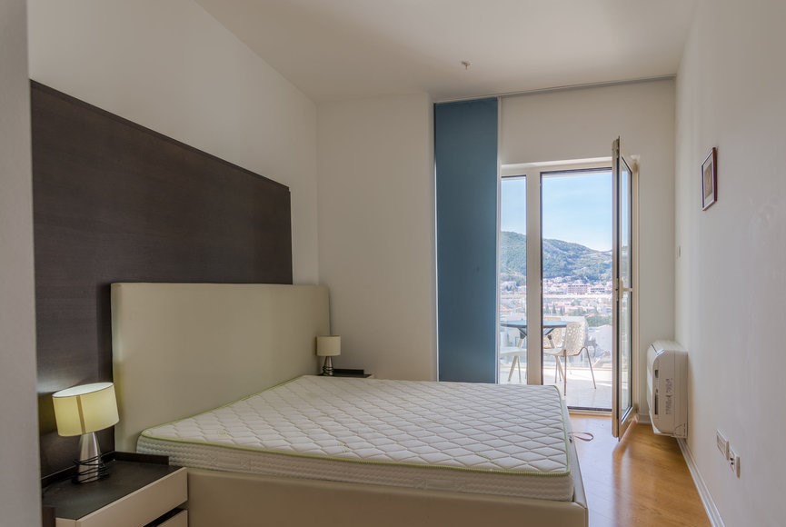 Bedroom in an apartment in Budva, Montenegro: a double bed, bedside tables, and access to a balcony with mountain views.