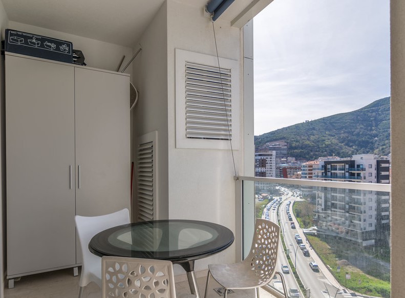 Balcony in an apartment in Budva, Montenegro: a dining area with a glass table and a view of the mountains and the city.