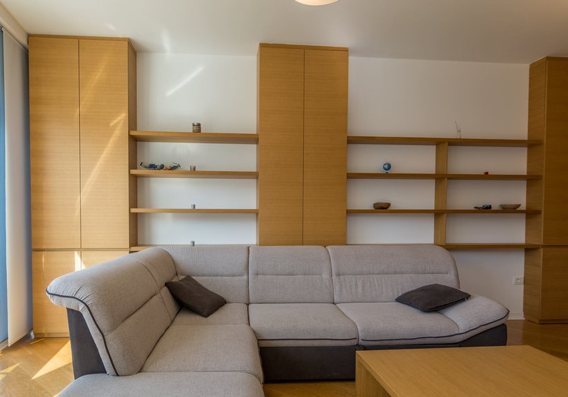 Living room with an L-shaped sofa and built-in wooden shelving in an apartment in Budva, Montenegro.