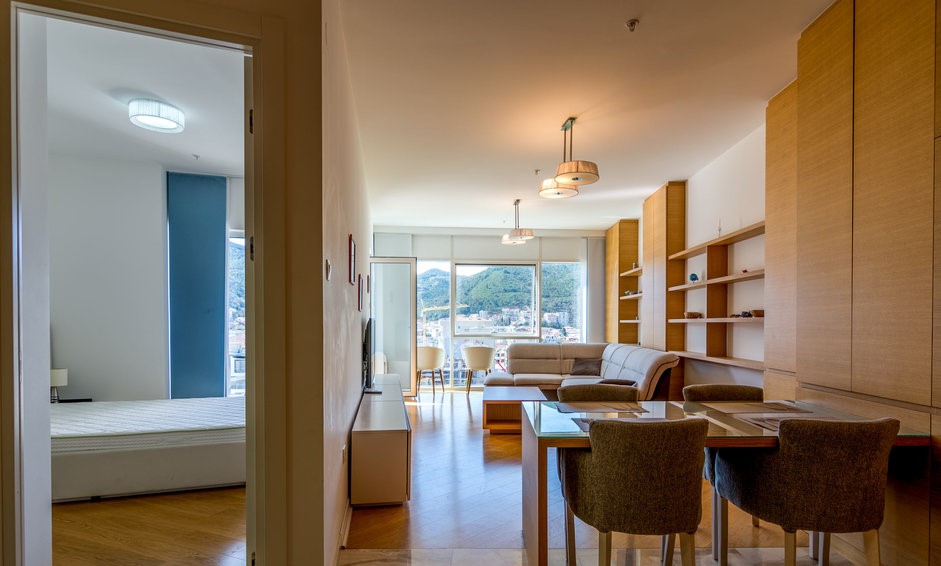 Living room interior with dining area in an apartment in Budva, Montenegro: modern furniture, mountain view, and parquet flooring.
