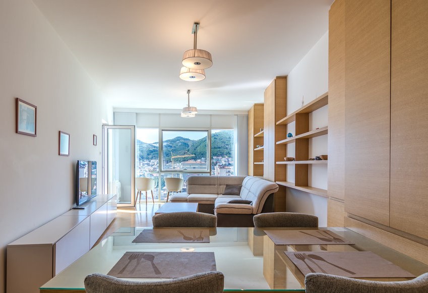 Modern living room with dining area in an apartment in Budva, Montenegro: light furniture, panoramic mountain view.