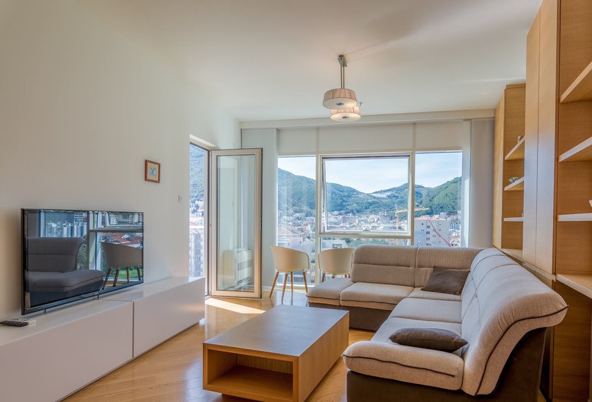 Modern living room in an apartment in Budva, Montenegro: corner sofa, panoramic windows with a view of the mountains and the city.