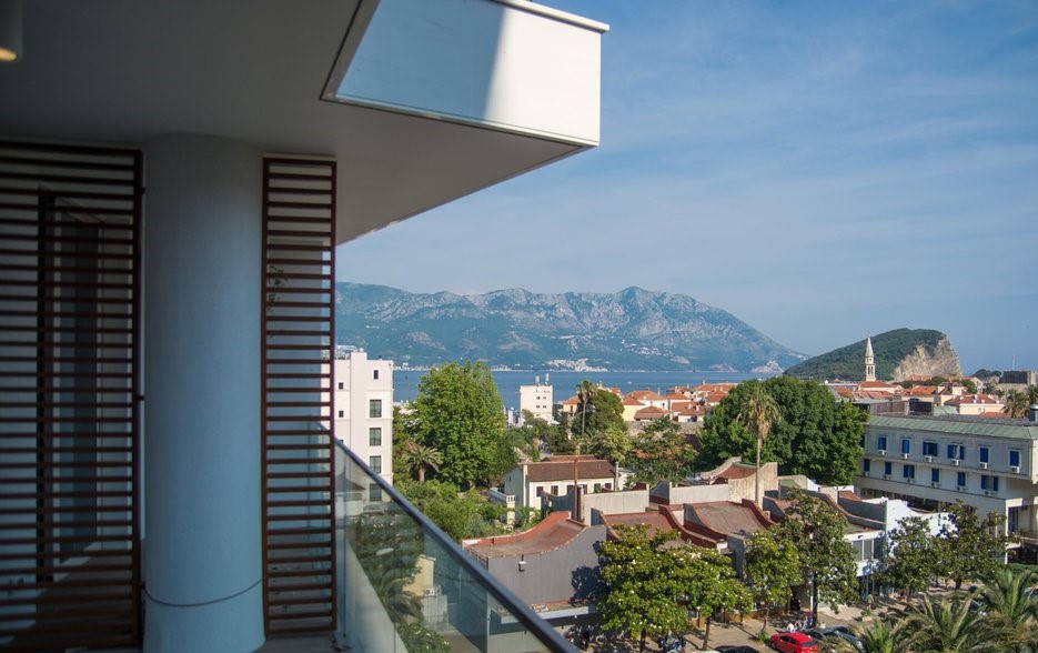 View from the balcony of a modern apartment in Budva, Montenegro: a panorama of the city, mountains, and the Adriatic Sea.